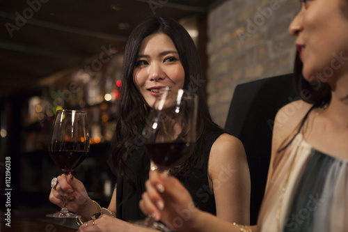 Two young women are drinking wine at the bar