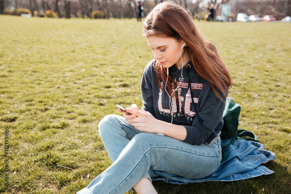 Obraz premium Woman listening to music from smartphone sitting on grass