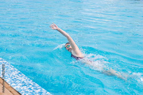 Young girl in goggles and cap swimming front crawl stroke style in the blue water pool © mr.markin