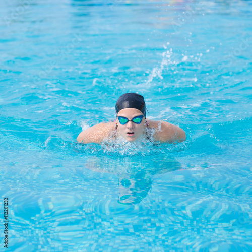 Young girl in goggles and cap swimming butterfly stroke style in the blue water pool © mr.markin