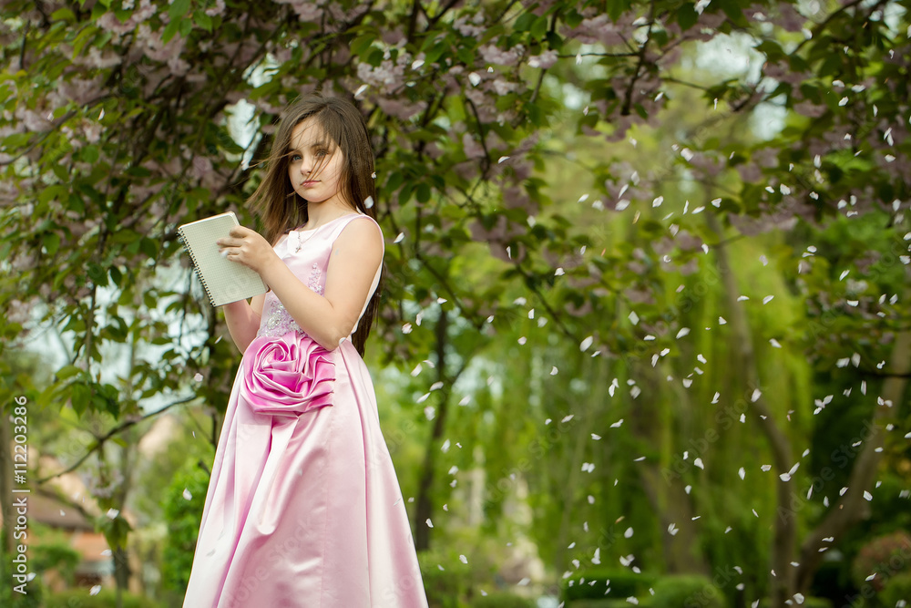 Girl in dress with notebook and pen in garden Girl in dress with notebook and pen in garden