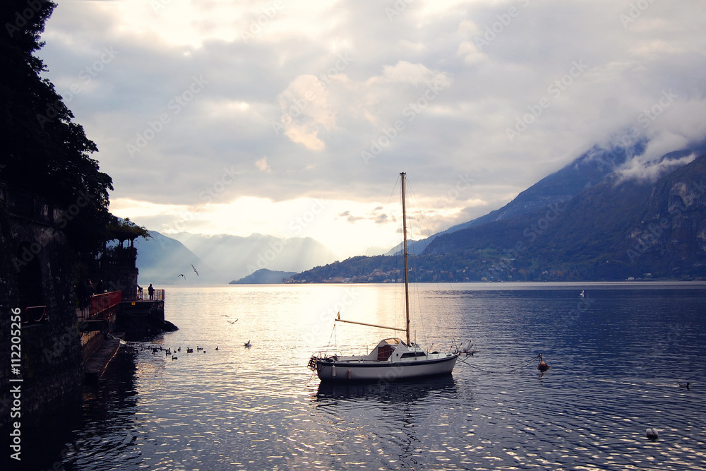 Fototapeta premium Boat on Lake Como at the sunset. Silver linings in Lake Como at the sunset. Retro style photo. Sunset view of the lake in Lombardy. Varenna, Lake Como, Italy.