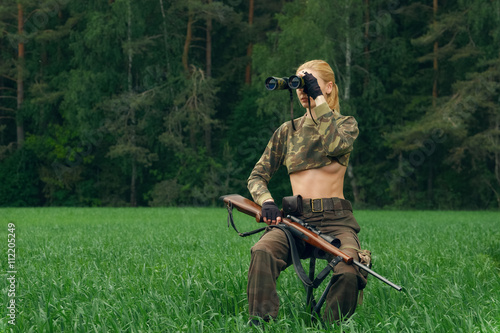 Attractive hunter girl with hunting carbine looking into binocul