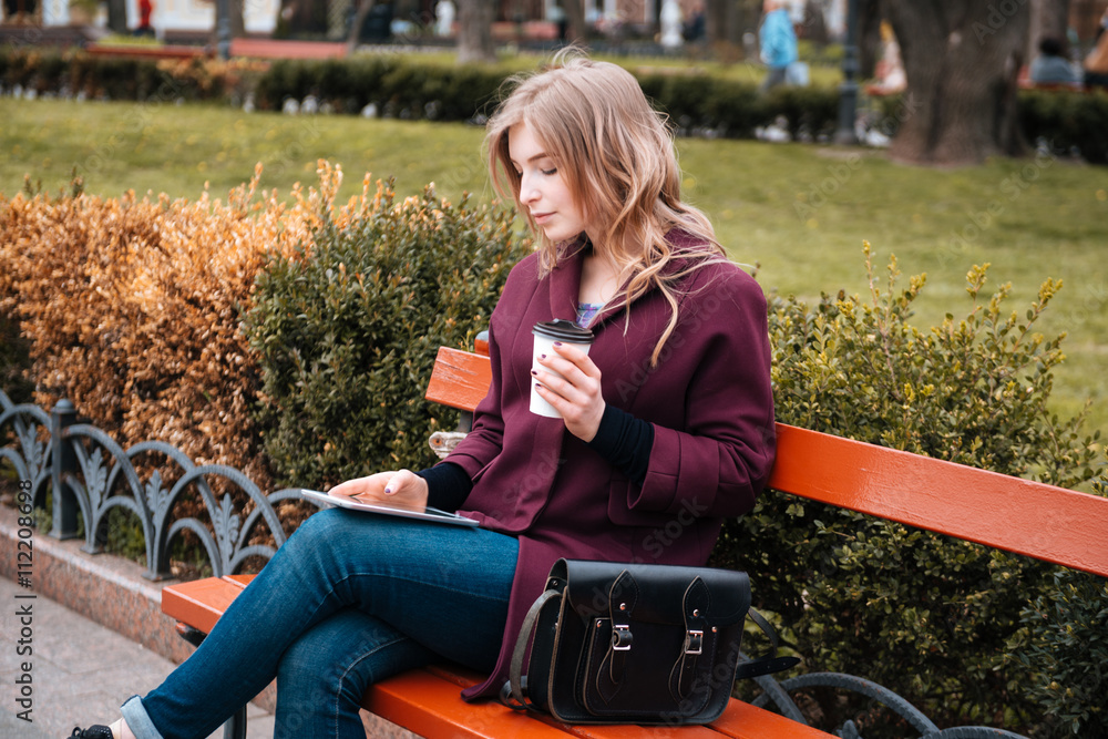 Thoughtful woman drinking coffee and using tablet in park Thoughtful woman drinking coffee and using tablet in park