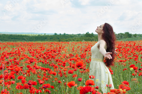Young beautiful woman walking through a poppy field, summer outdoor