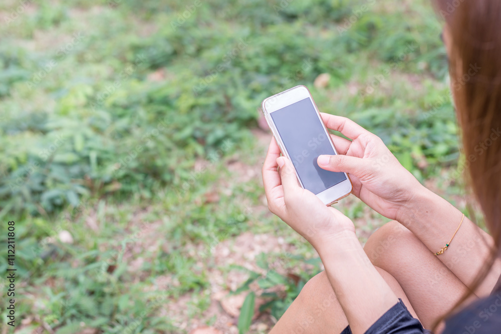 Asian woman with smartphone outdoors in park. Closeup of female hand Asian woman with smartphone outdoors in park. Closeup of female hand