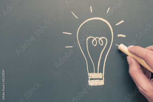 Hand writing light bulb on blackboard