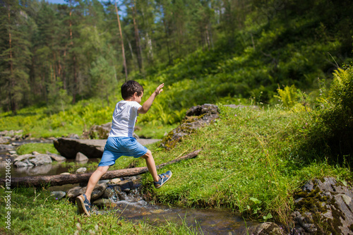 Little boy jumps over a stream in a forest