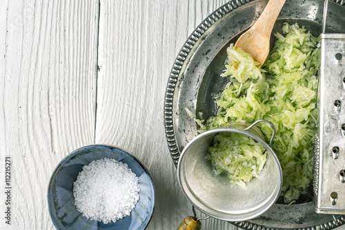 Grated cucumber with strainer and salt on the white table  top view