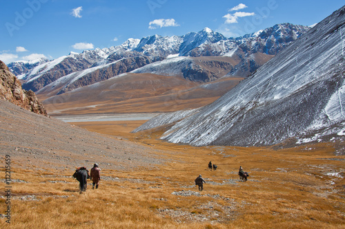 Hunters with horses descend from the mountains into the valley.