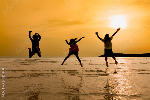 Silhouette of 3 little asian girls jumping on  beach at sunset i