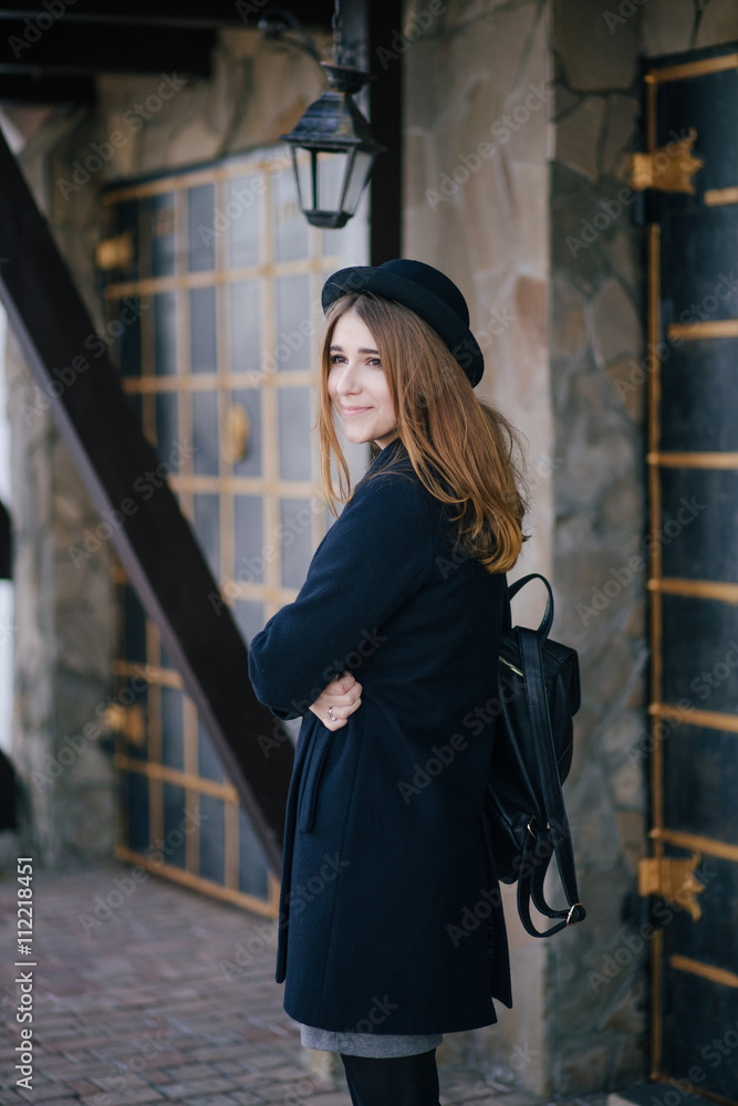 Beautiful young woman wearing hat and dark-blue coat walking on a city street Beautiful young woman wearing hat and dark-blue coat walking on a city street