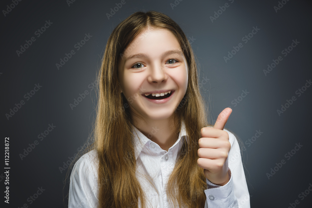 Happy girl. Closeup Portrait of handsome teen in casual shirt smiling show thumb up on grey background Happy girl. Closeup Portrait of handsome teen in casual shirt smiling show thumb up on grey background