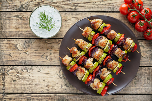 Turkey or chicken meat shish kebab skewers with tzatziki sauce and tomatoes on rustic wooden table background. Traditional barbecue grill food photo