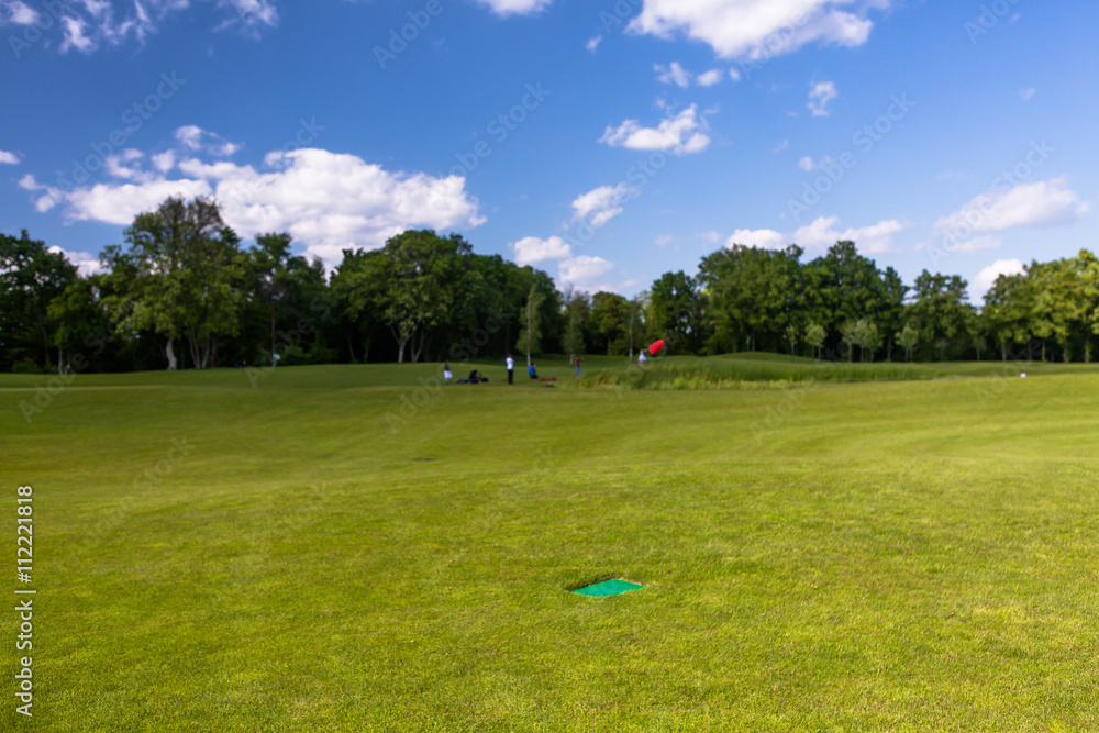 Golf course in countryside with people on background. Golf course putting green with flag in spring or summer colors. Golf course in countryside with people on background. Golf course putting green with flag in spring or summer colors.
