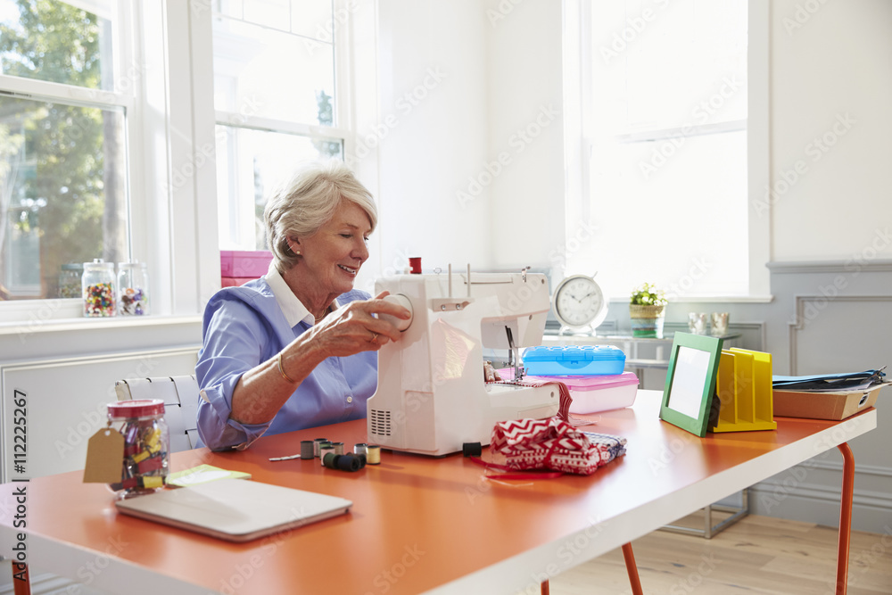 Senior Woman Making Clothes Using Sewing Machine At Home Senior Woman Making Clothes Using Sewing Machine At Home