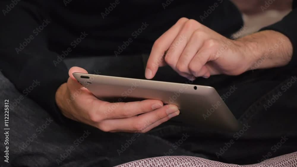 Fingers of a man using a tablet device in bed at home. Fingers of a man using a tablet device in bed at home.