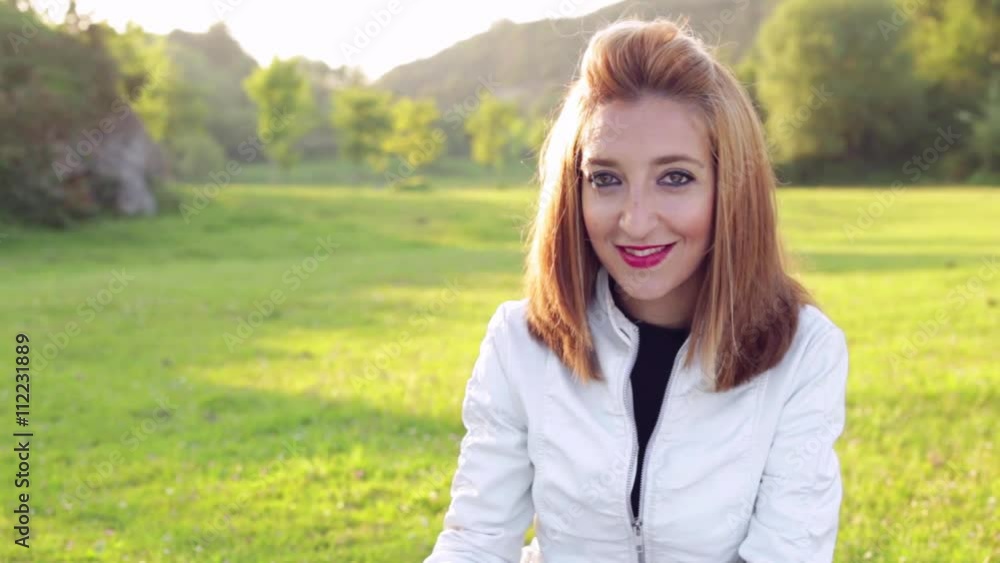 Woman outdoors in a park, looking at camera, while reading a book.