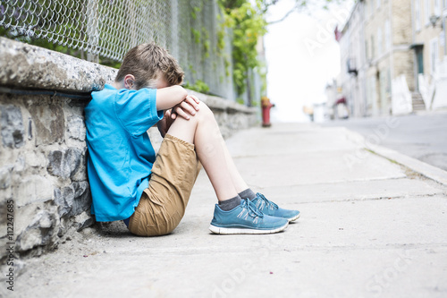 Photo of Sad and Stressed Kid sit by the Wall outdoor