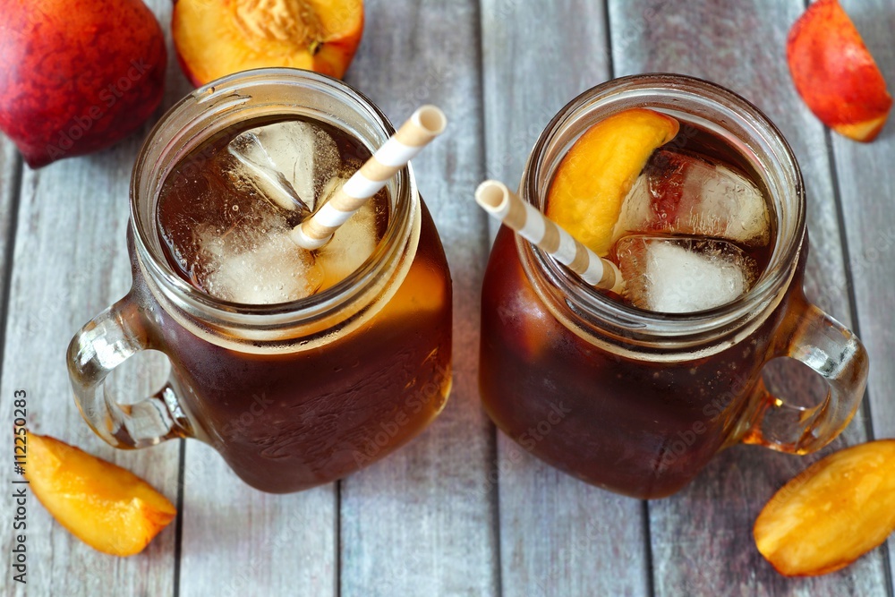 Two mason jar glasses of homemade peach iced tea on a rustic wood background, downward view Two mason jar glasses of homemade peach iced tea on a rustic wood background, downward view