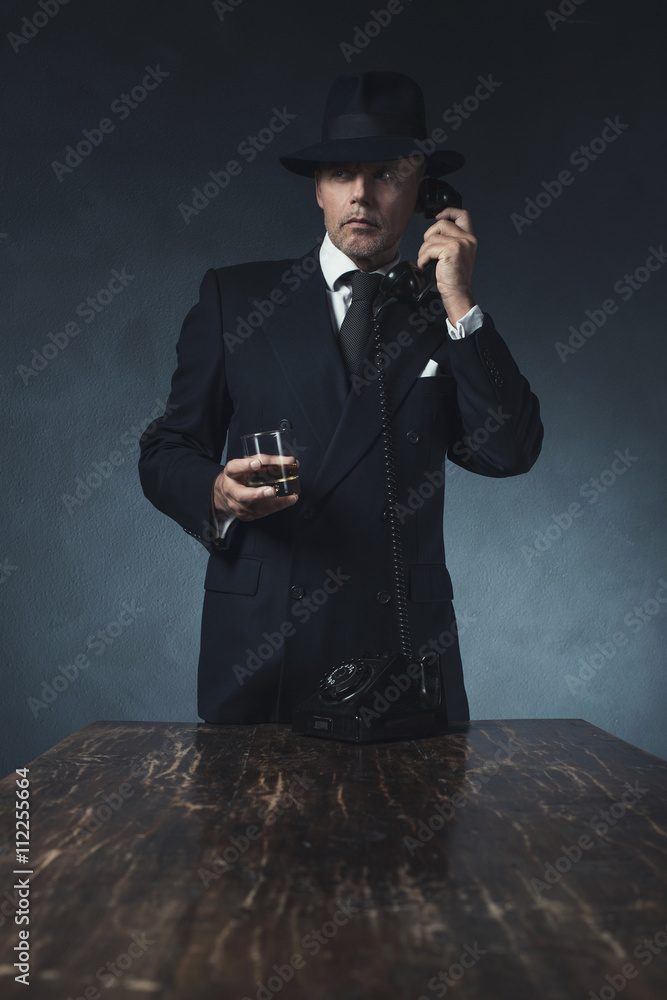 Retro 1940 businessman on the phone with glass of whiskey. Stand
