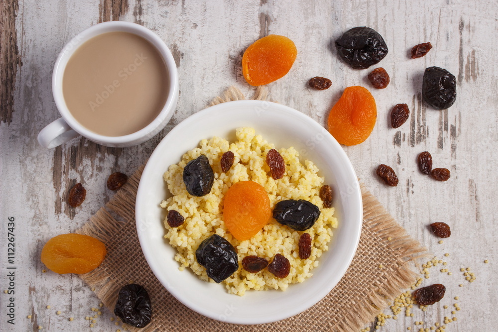 Cooked millet groats on white plate and cup of coffee with milk, healthy food and nutrition Cooked millet groats on white plate and cup of coffee with milk, healthy food and nutrition