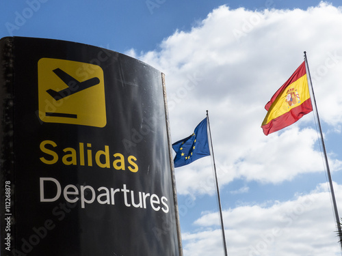 Signpost departure with Spanish and European flag in background.