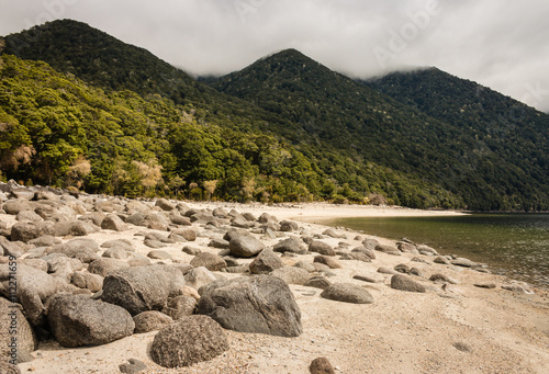 boulders on white sand beach at lake Manapouri in New Zealand