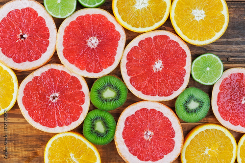 Slices of red grapefruit  lime  orange  and kiwi arranged on rustic wooden table closeup. Top view.