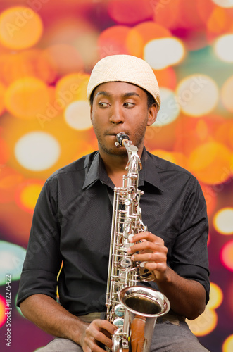 African man wearing sixpence hat and dark shirt playing saxophone, facing camera photo