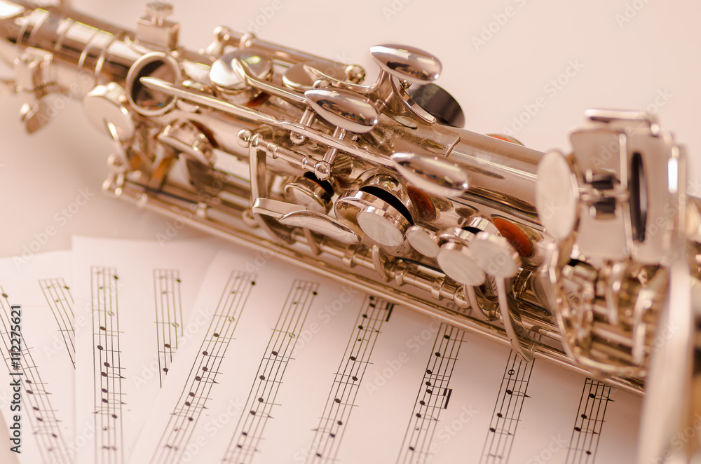Obraz premium Closeup partly view of shiny saxophone lying on musical notes paper