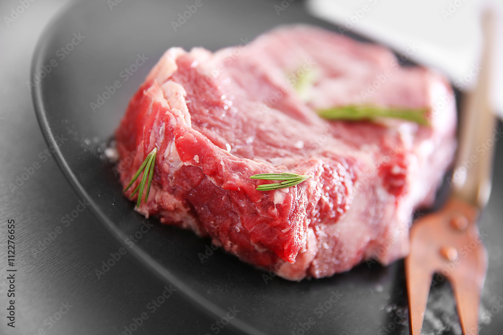 Raw pork steak with meat fork and rosemary on black plate