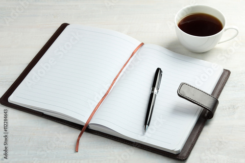 Notepad with pen on white wooden background with Cup of strong coffee