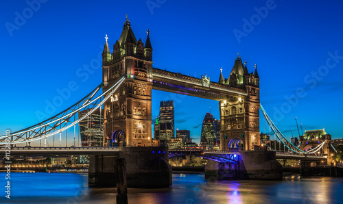Illuminated Tower Bridge in London after sunset with London   s financial district at the background