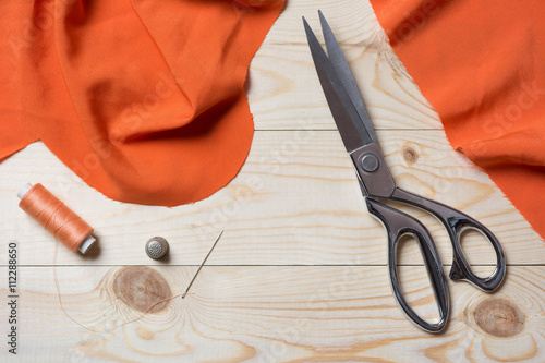 Cutting orange fabric with a taylor scissors on wooden table