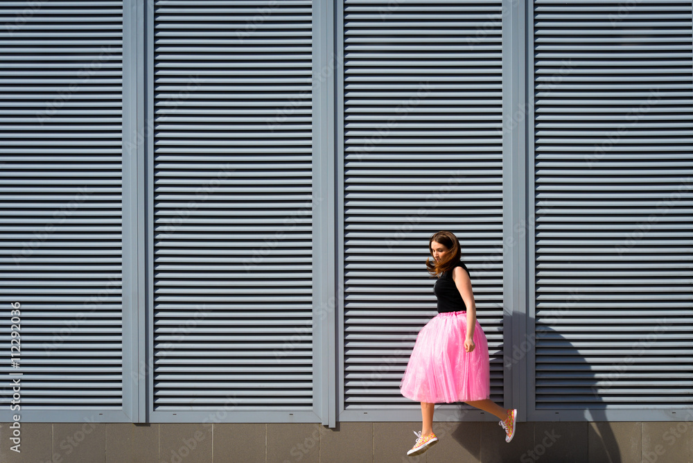 Beautiful sexy young hipster girl jumping outdoors.Posh woman with long brunette hair evening makeup wearing light fluffy pink rosy skirt and vans sneakers posing in the city urban style in summer Beautiful sexy young hipster girl jumping outdoors.Posh woman with long brunette hair evening makeup wearing light fluffy pink rosy skirt and vans sneakers posing in the city urban style in summer