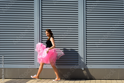Beautiful sexy young hipster girl outdoors.Posh woman with long brunette hair evening makeup wearing light fluffy pink rosy skirt and vans sneakers posing outdoors in the city urban style in summer © ISOstudio