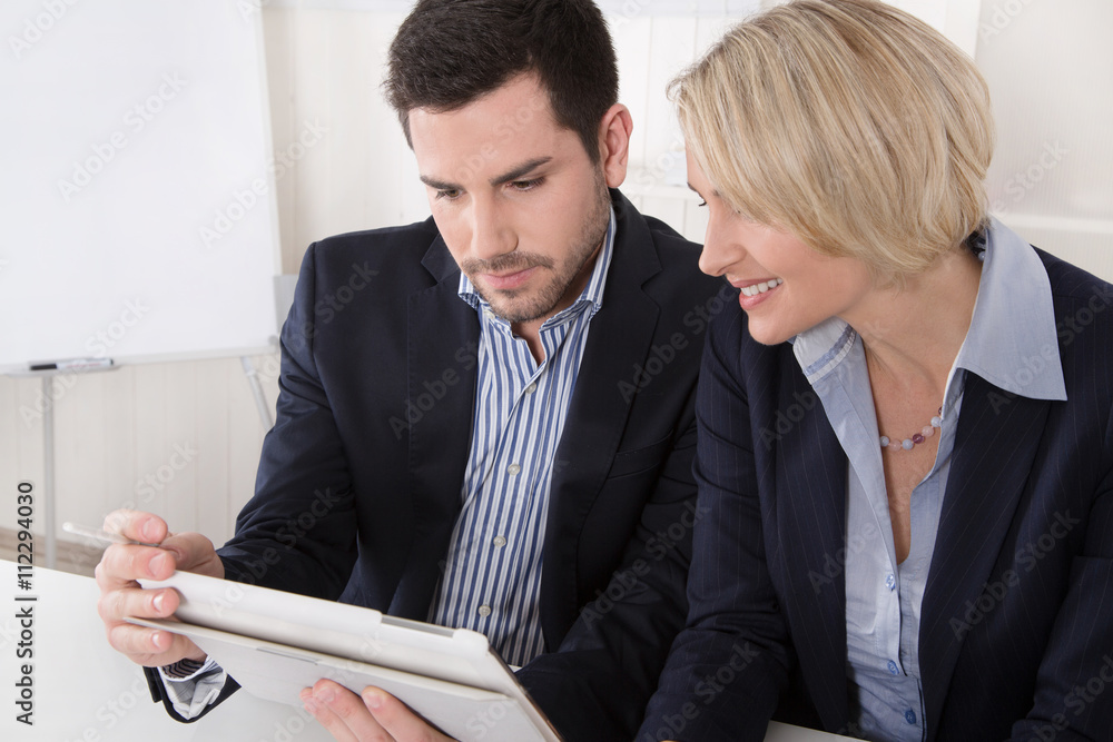 Zwei Personen sitzen im Büro in einem Meeting und blicken auf ein ...