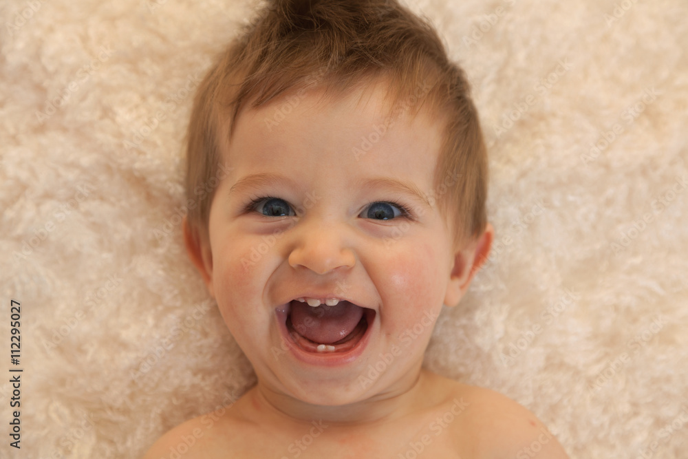 Portrait of a one year old boy with blue eyes and blonde hair. Laying down and laughing Portrait of a one year old boy with blue eyes and blonde hair. Laying down and laughing