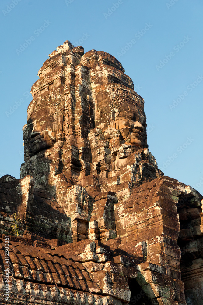 Fototapeta premium Dramatic view at sunset of one of the many large stone carved faces of Bayon Temple in Angkor Thom, Angkor district, Siem Reap, Cambodia