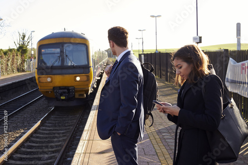 Commuters Waiting On Railway Platform Using Mobile Phones