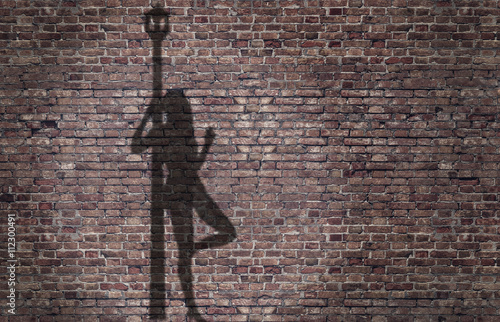ombra di una prostituta appoggiata al lampione sul muro di mattoni  photo