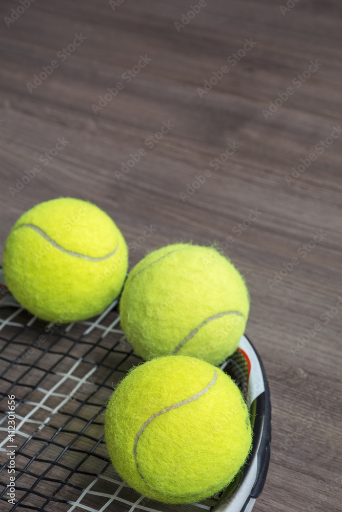 Usual tennis racquet with three green balls on the wooden background