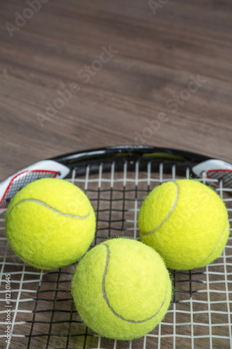 Tennis racquet with three green balls on the wooden background © Anastasia Pestova