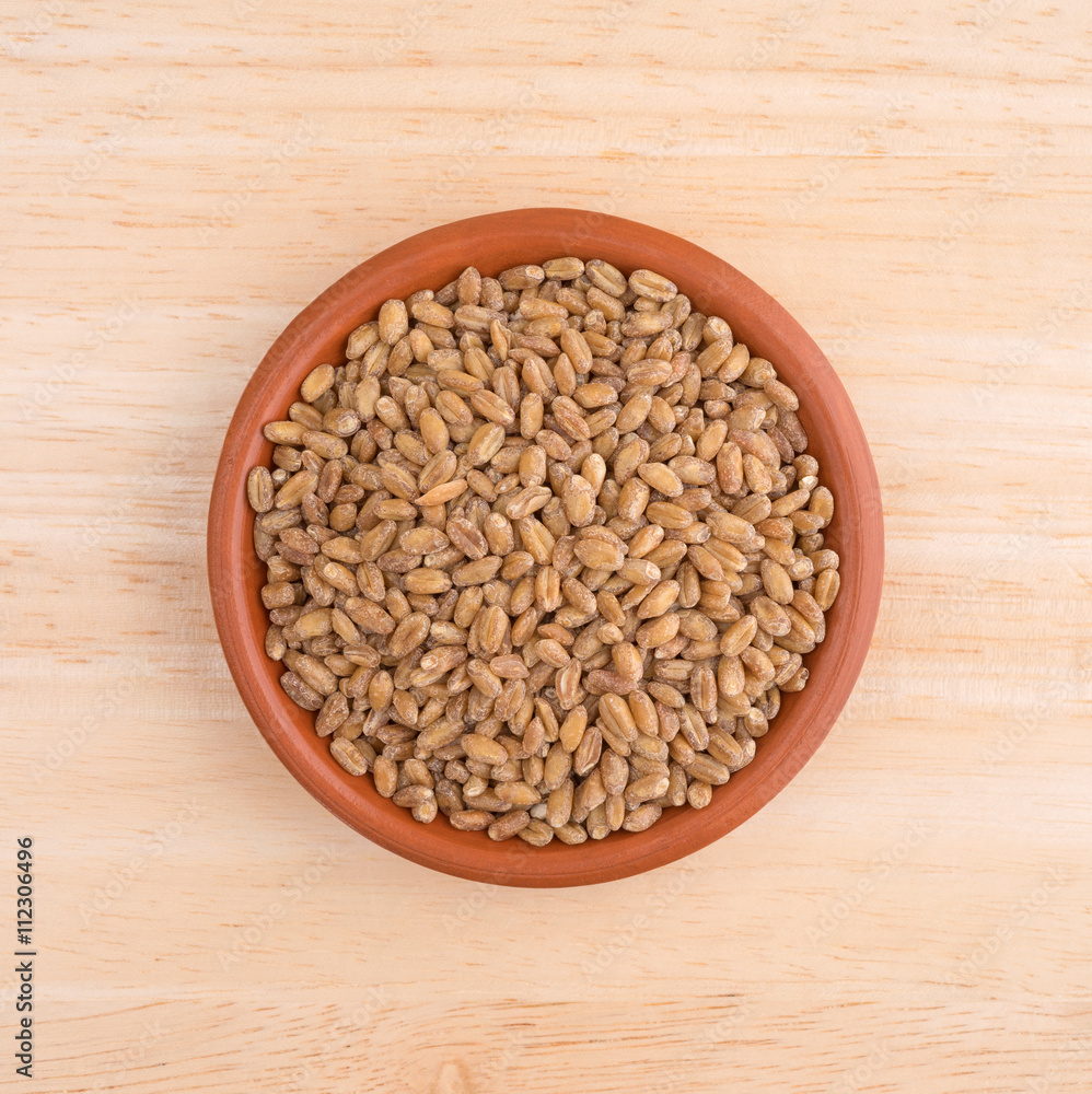 Small bowl of red winter wheat berries on wood table