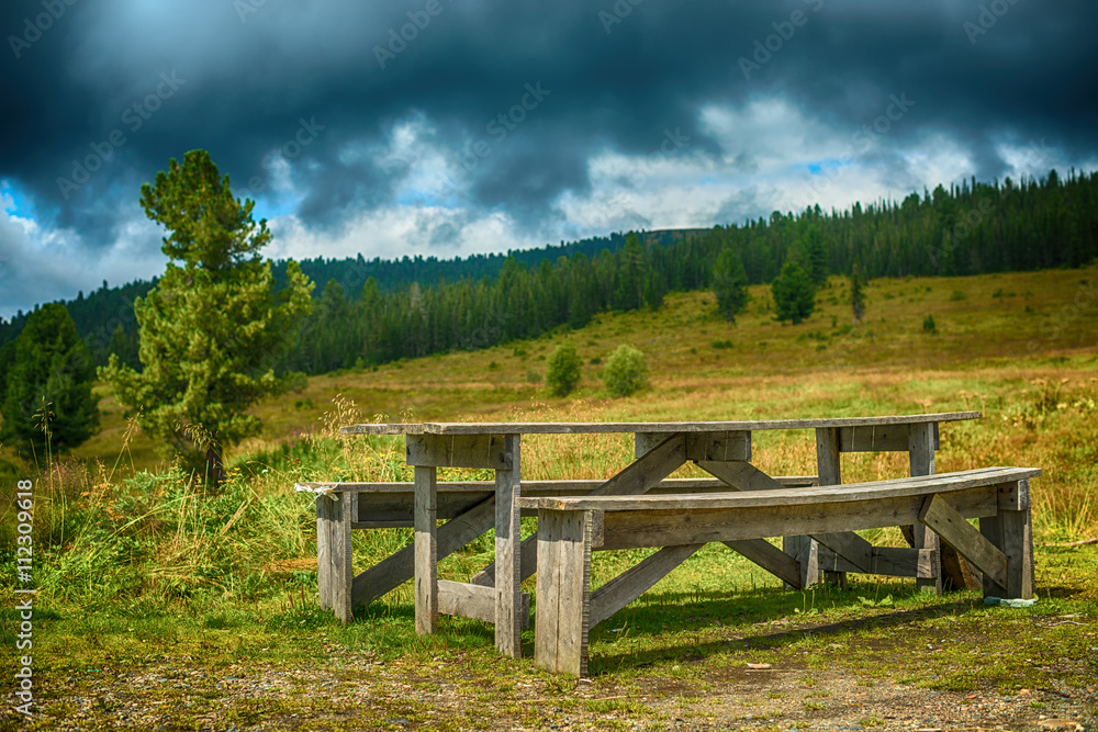 wooden bench and table in the woods on a background of mountains
wooden bench and table in the woods on a background of mountains