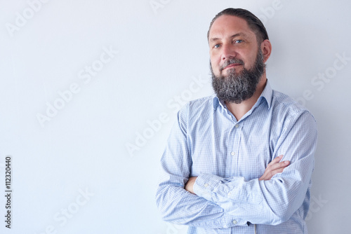 Mature male with beard and arms crossed against white wall