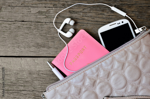 Set of female accessories looks out of the bag. Passport, pen, phone, headphones on a wooden background