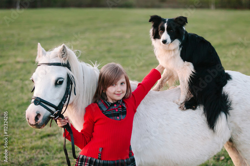 Little baby girl in red dress. Dog on horseback. A small white pony