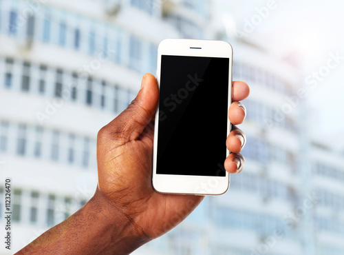 Hand shows mobile smart phone, urban city blurred background